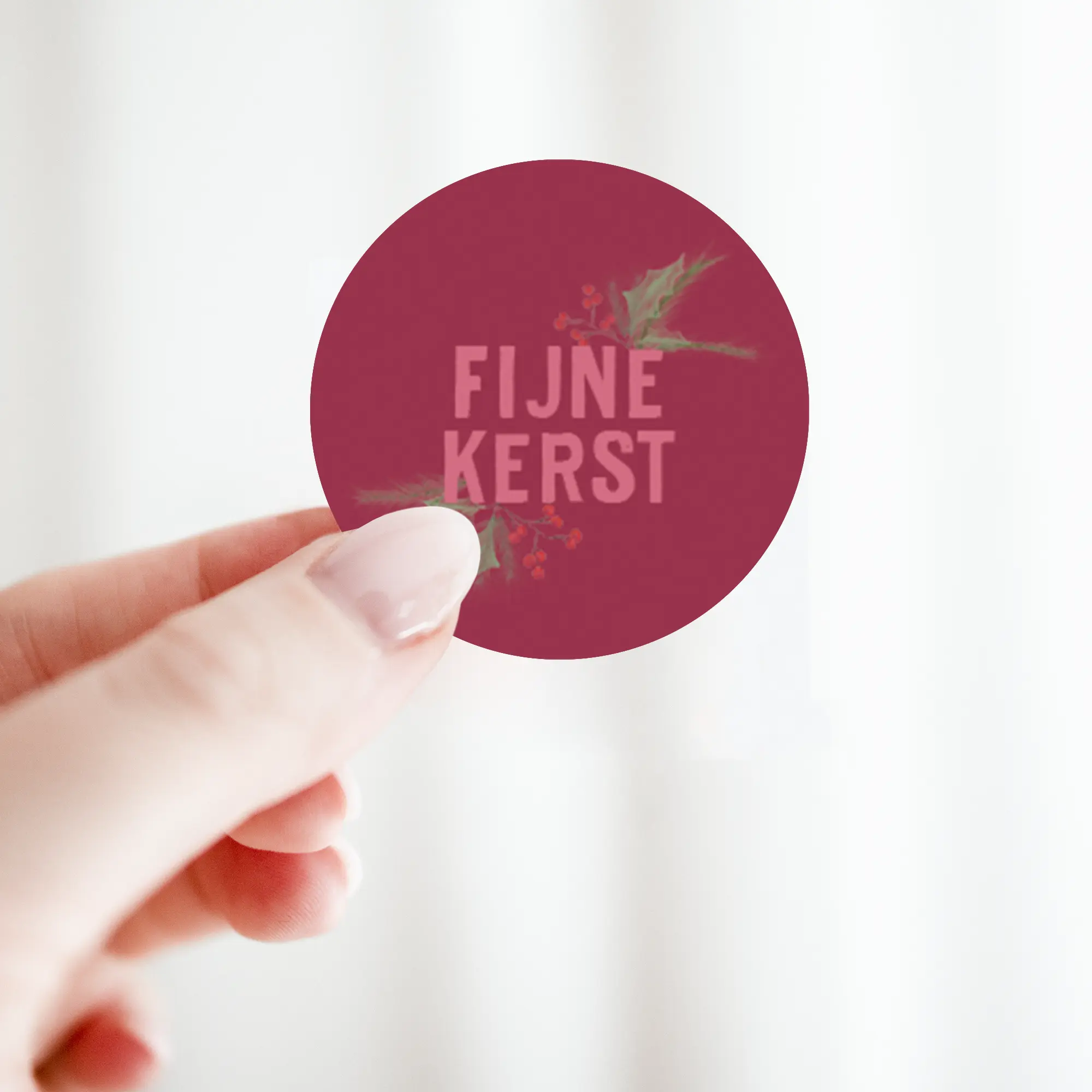 Sticker ‘Fijne kerst’ in bordeaux en roze tinten, vastgehouden in de hand
