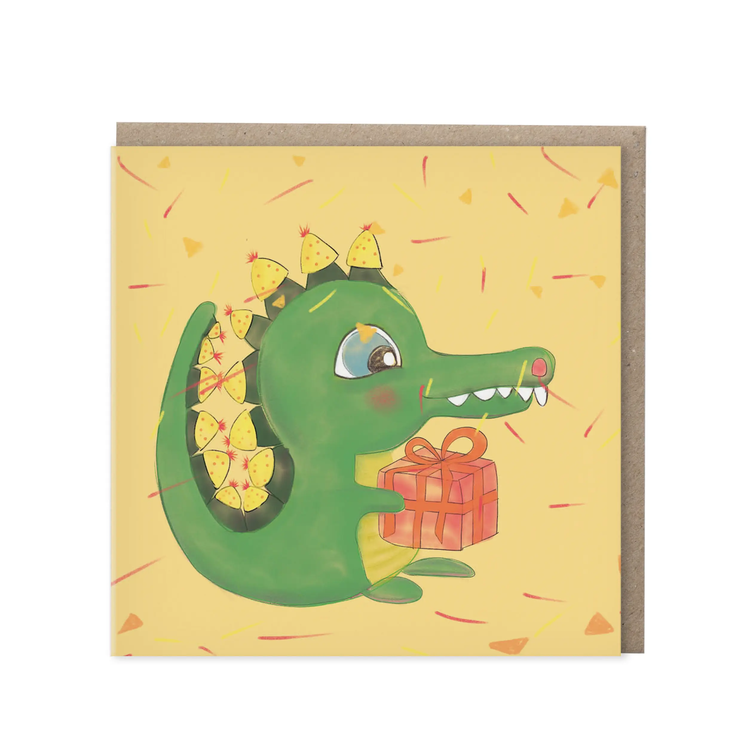 Vierkante wenskaart met een vrolijke groene krokodil met feesthoedjes op zijn rugstekels en een rood cadeautje op een gele achtergrond vol confetti, met kraft envelop op de achtergrond