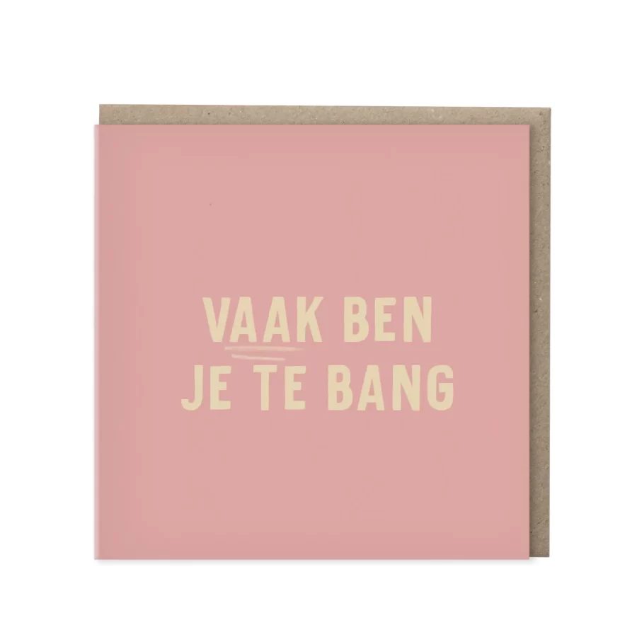 Vierkante roze wenskaart met de tekst Vaak ben je te bang in crèmekleurige blokletters, met kraft envelop op de achtergrond